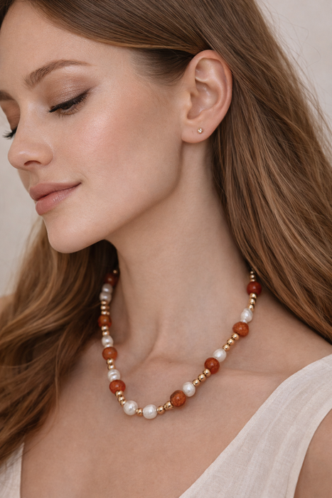 Woman wearing a pearl and brown bead necklace with a neutral background