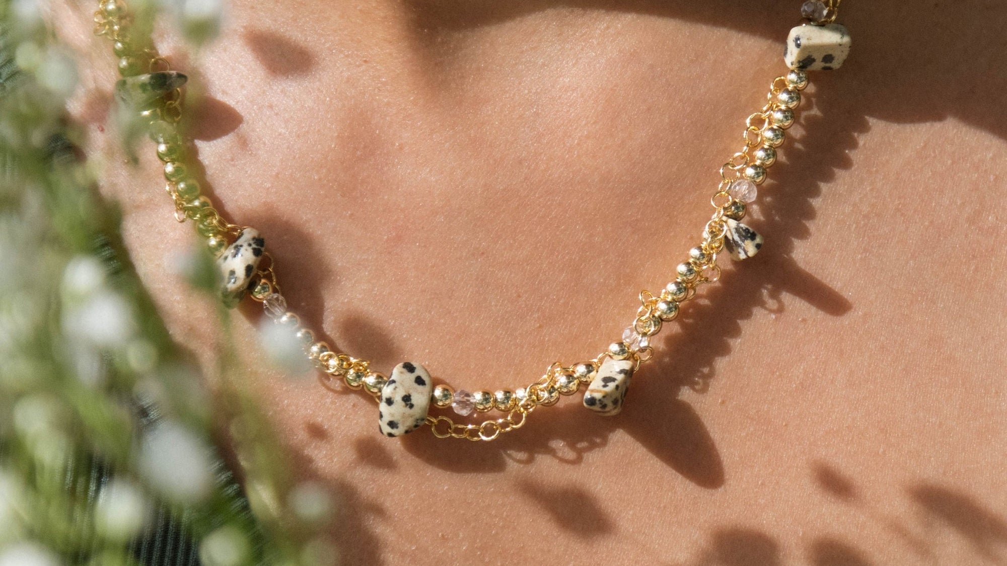Close-up of a person wearing a gold necklace with green beads, surrounded by greenery.