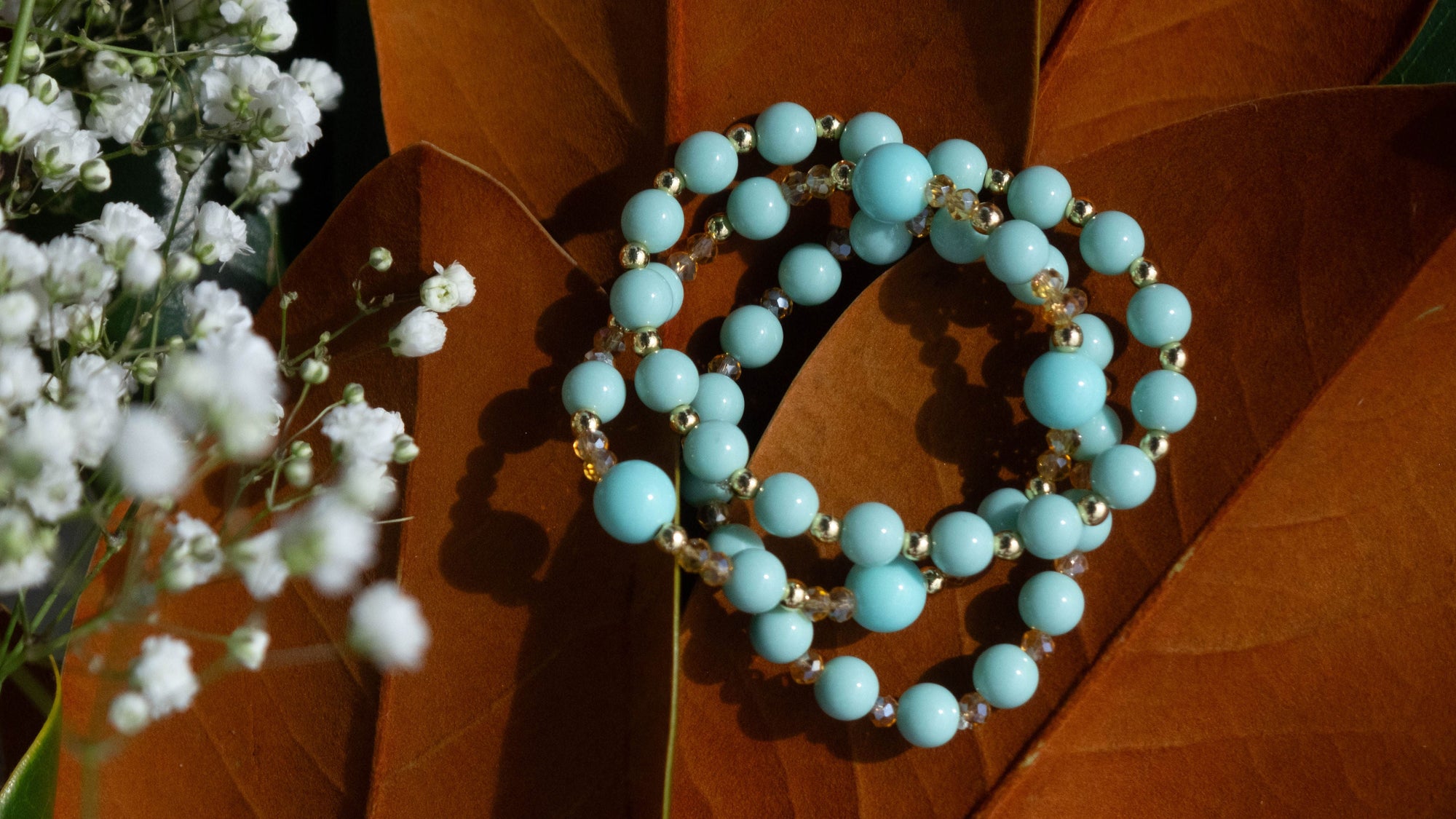 Turquoise beaded bracelet on a brown leaf with white flowers in the corner