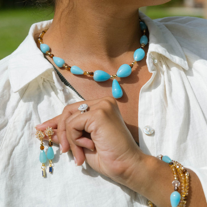 Person wearing turquoise beaded jewelry with a blurred green background