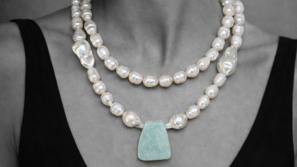 Woman wearing a pearl necklace with a large turquoise pendant against a neutral background