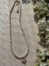 Pearl necklace with a diamond pendant on a textured surface with flowers