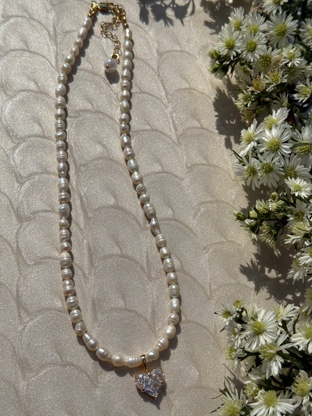 Pearl necklace with a diamond pendant on a textured surface with flowers