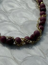 Necklace with purple beads and gold chain on a textured white background