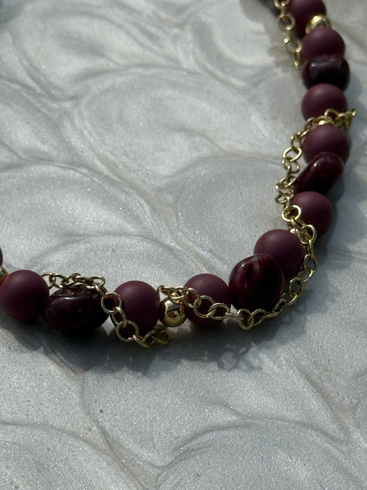 Necklace with purple beads and gold chain on a textured white background