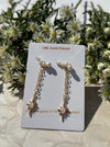 Gold-plated earrings with pearls on a card, surrounded by greenery