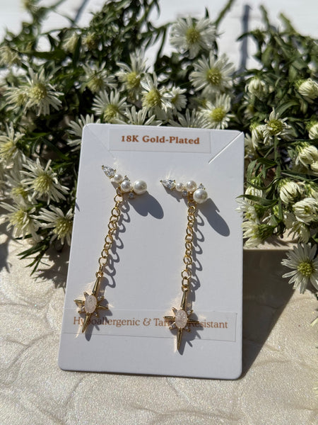 Gold-plated earrings with pearls on a card, surrounded by greenery