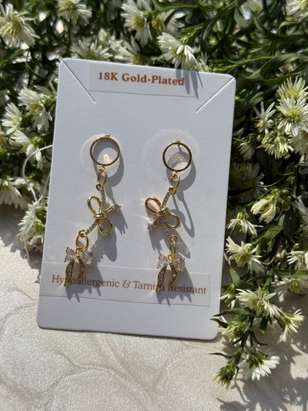 Gold-plated bow-shaped earrings on a card with floral background