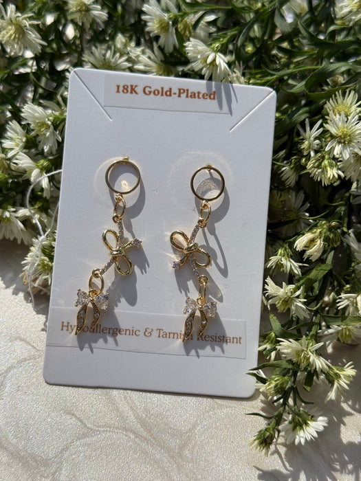 Gold-plated bow-shaped earrings on a card with floral background