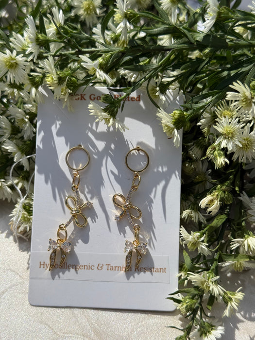 Gold bow-shaped earrings on a card with floral background