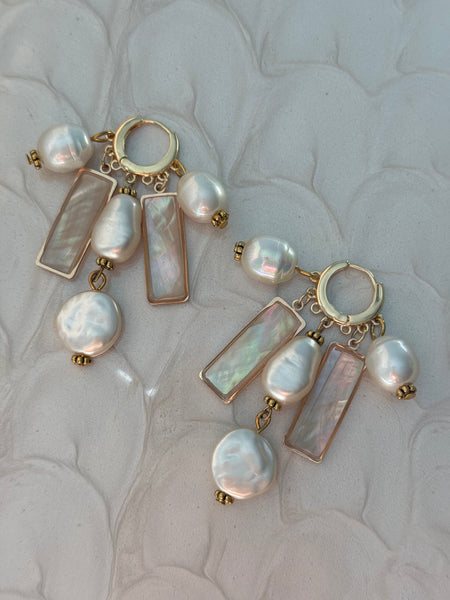 Pearl and gold earrings on a textured beige background