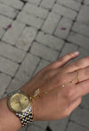 Hand wearing a gold watch and bracelet on a blurred pavement background