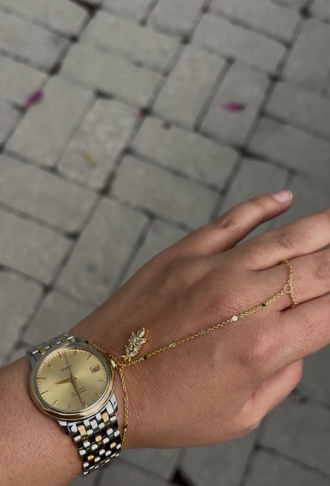 Hand wearing a gold watch and bracelet on a blurred pavement background