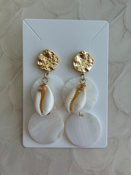 Pair of earrings with gold accents and cowrie shell elements on a white card.