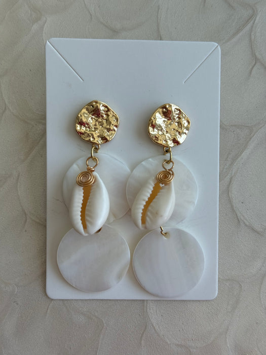Pair of earrings with gold accents and cowrie shell elements on a white card.