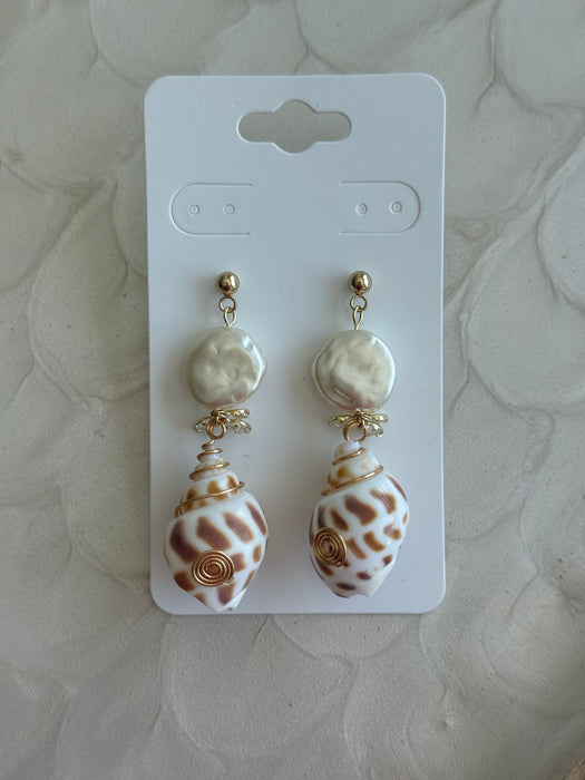 Shell-shaped earrings on a white card with a textured beige background