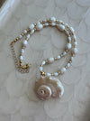 Necklace with shell pendant and gold beads on a textured white surface