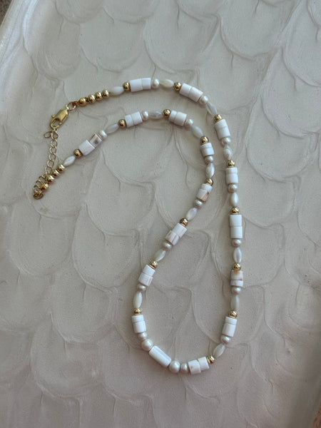 Necklace with white beads and gold accents on a textured beige background