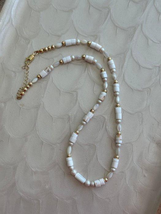 Necklace with white beads and gold accents on a textured beige background