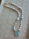 Pearl necklace with a turquoise pendant on a textured beige surface