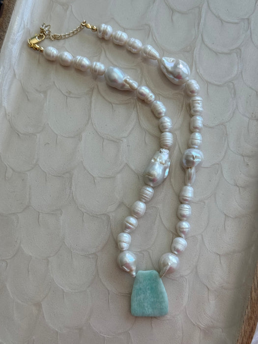 Pearl necklace with a turquoise pendant on a textured beige surface