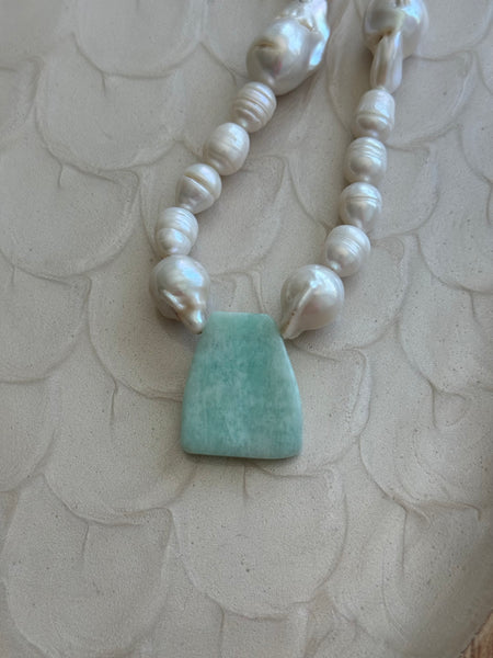 Necklace with white beads and a green stone on a textured beige background