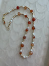 Necklace with red, white, and gold beads on a textured beige background