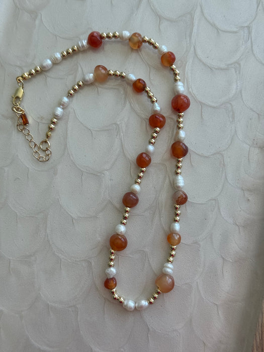 Necklace with red, white, and gold beads on a textured beige background