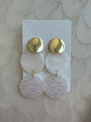 Pair of gold and pink earrings on a white card against a beige background