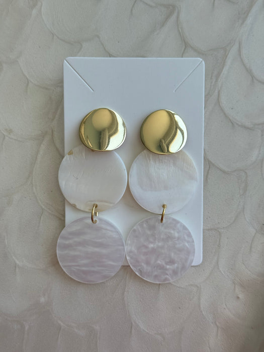 Pair of gold and pink earrings on a white card against a beige background