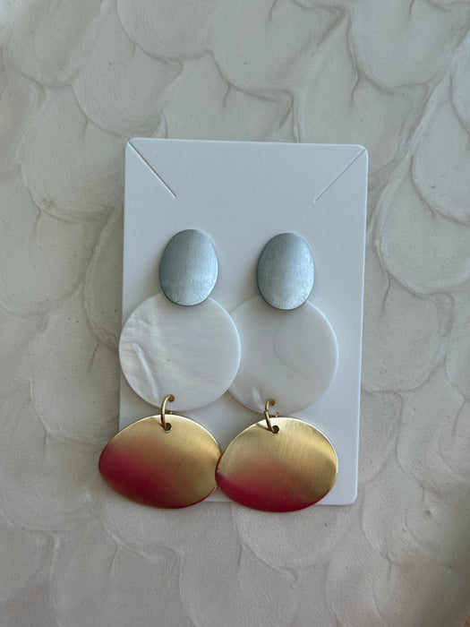 Pair of earrings with gold and red gradient on a white card against a textured beige background