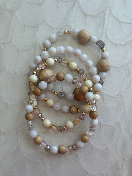 Beaded bracelets with white, brown, and clear beads on a textured beige background