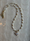 Pearl necklace with a heart-shaped crystal pendant on a textured white background