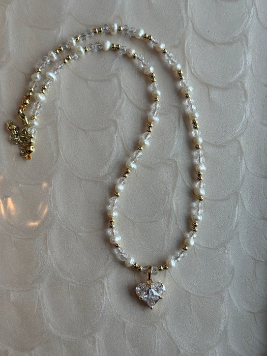 Pearl necklace with a heart-shaped crystal pendant on a textured white background