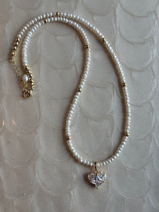Pearl necklace with a heart-shaped pendant on a textured beige background
