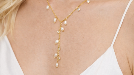 Woman wearing a gold necklace with pearl-like beads against a blurred background